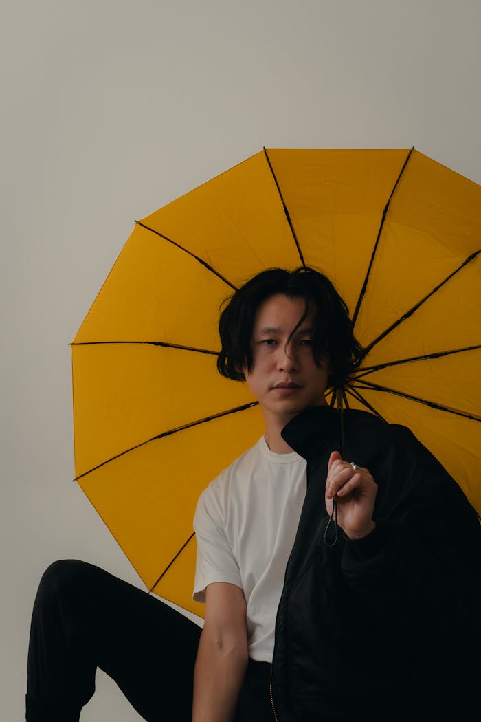 Fashion portrait of a man holding a yellow umbrella in a studio setting.